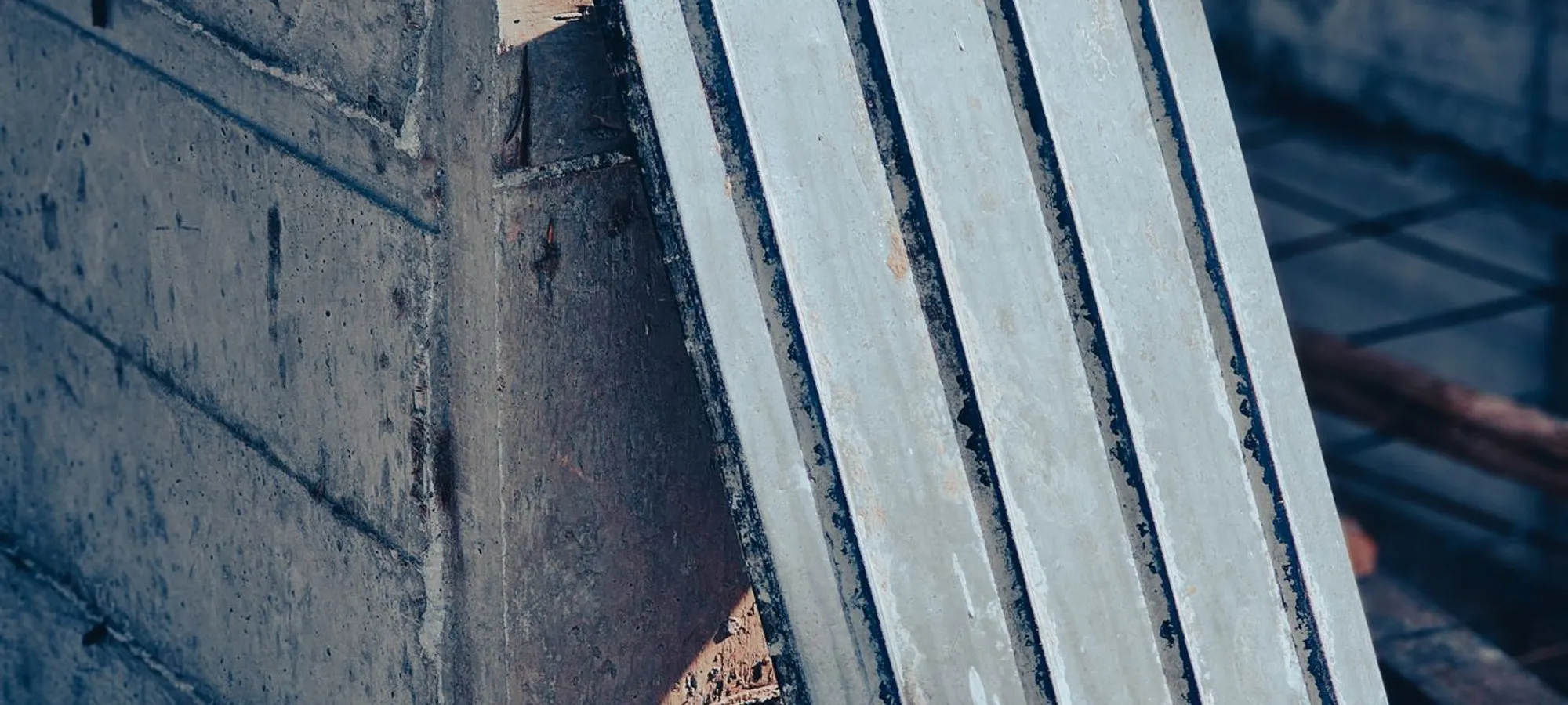 Precast concrete planks leaning against a poured concrete wall, the ribbed profile of the planks catching low sunlight