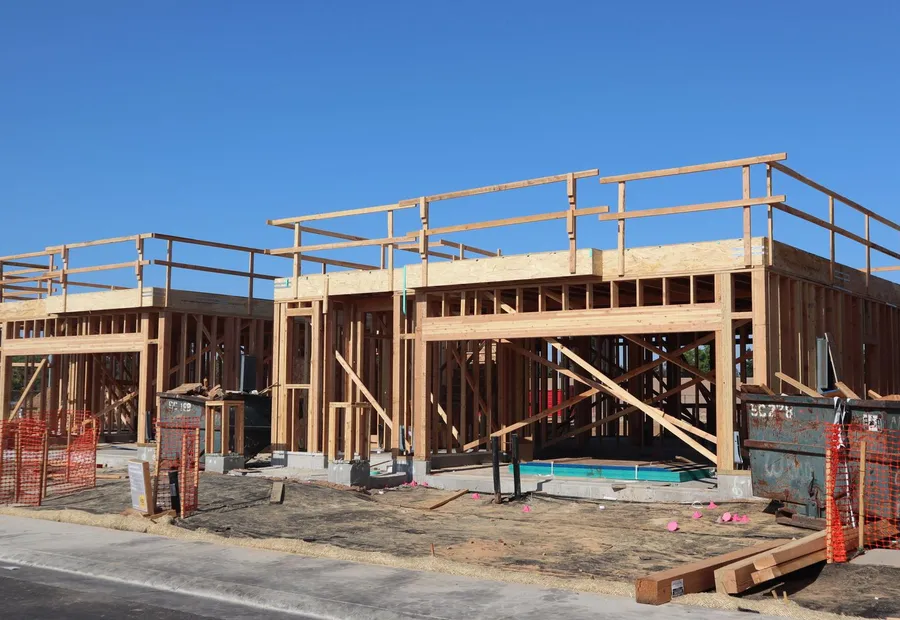 Two adjacent house frames at first floor level with let-in diagonal bracing and orange safety fencing around the perimeter